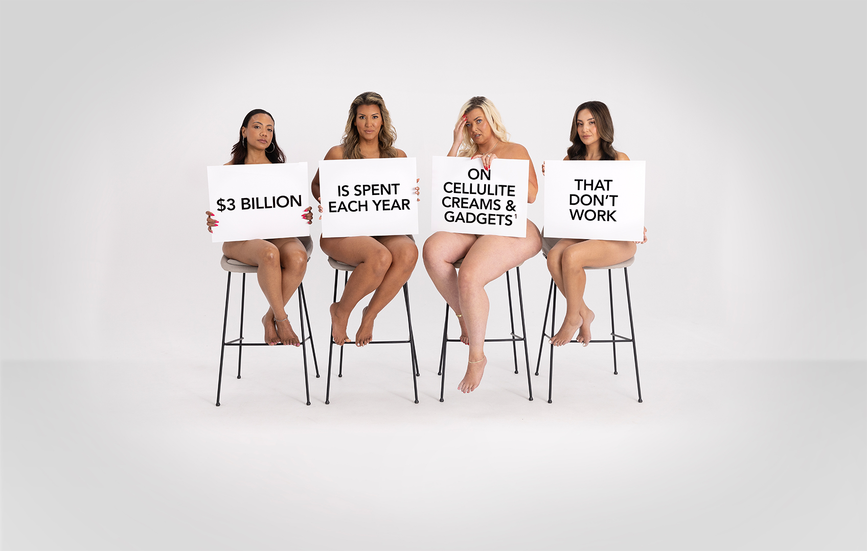 Four women sitting on stools holding posters that say "$3 Billion is spent each year on cellulite creams & gadgets that don't work"